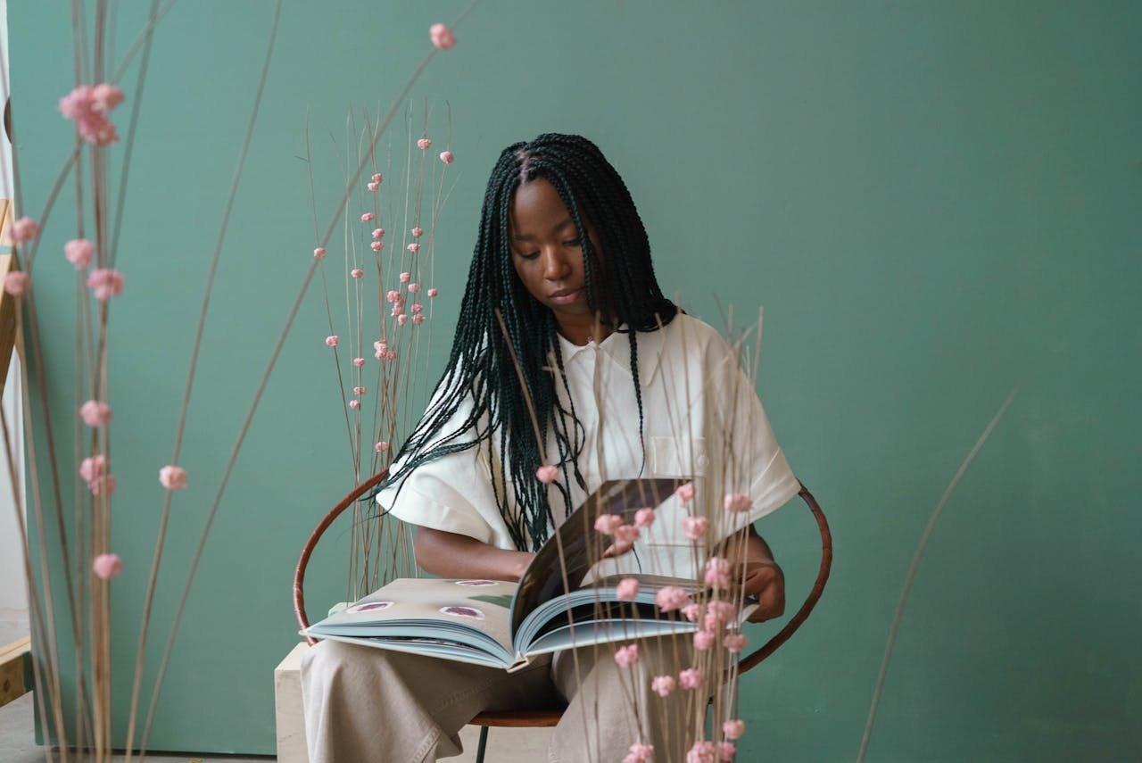 Smart African American lady reading magazine on chair in room